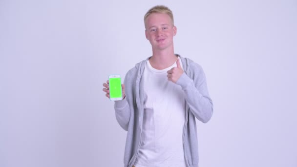 Happy young blonde man showing phone and giving thumbs up - Séquence, vidéo
