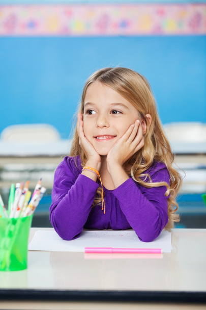 Girl Smiling While Sitting With Head In Hands At Desk - Фото, изображение