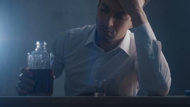 落ち込んだビジネスマンは、暗い部屋で一人で飲むショットグラスにウイスキーを注ぎます。アルコール依存症の概念. - 映像、動画