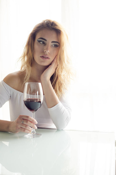 Joven hermosa mujer con copa de vino tinto sobre fondo claro
  - Foto, imagen