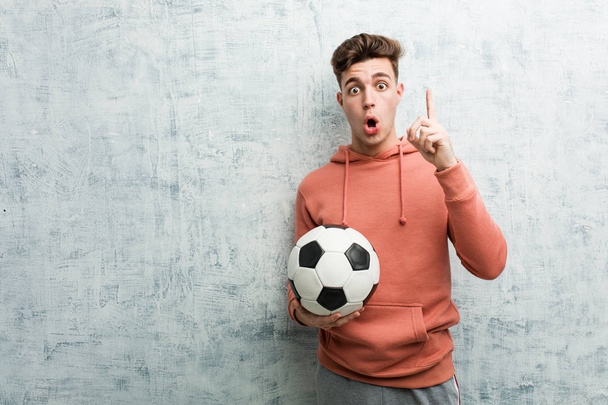 Νεαρός αθλητικός άνδρας κρατώντας μια μπάλα ποδοσφαίρου έχει κάποια μεγάλη ιδέα, έννοια της δημιουργικότητας. - Φωτογραφία, εικόνα