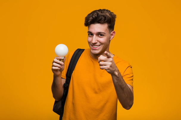Young student man holding a light bulb shouting excited to front. - Photo, Image