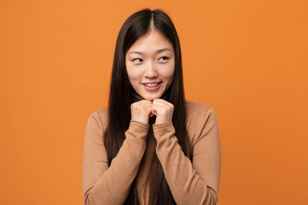Mladá krásná Číňanka drží ruce pod bradou, šťastně se dívá stranou. - Fotografie, Obrázek