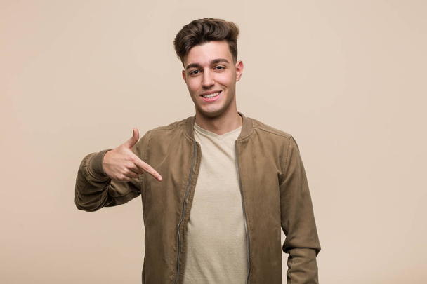 Jovem caucasiano vestindo uma pessoa jaqueta marrom apontando à mão para um espaço de cópia camisa, orgulhoso e confiante
 - Foto, Imagem