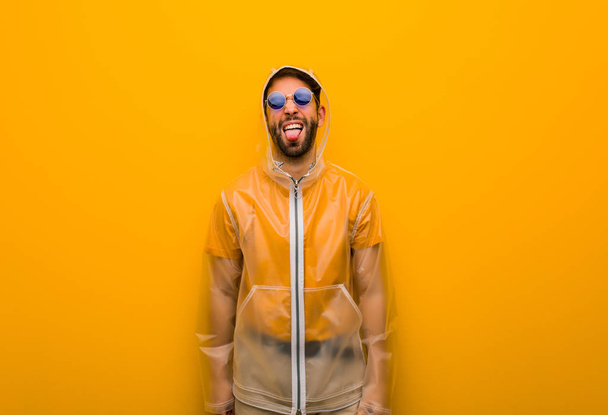 Young man wearing a rain coat funnny and friendly showing tongue - Φωτογραφία, εικόνα