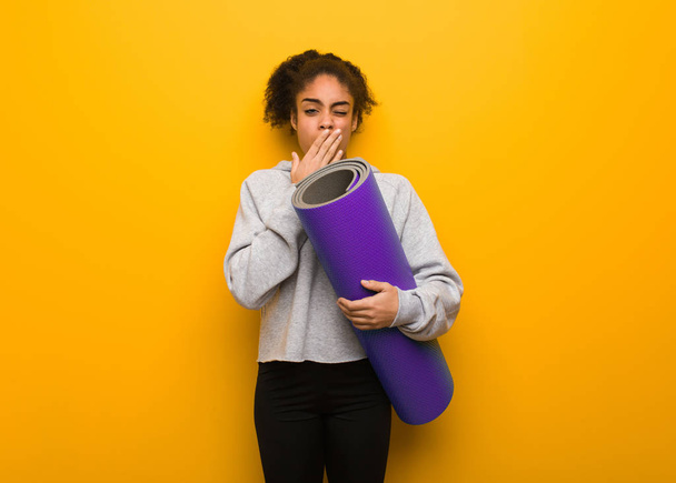 Young fitness black woman tired and very sleepy. Holding a mat. - Photo, Image