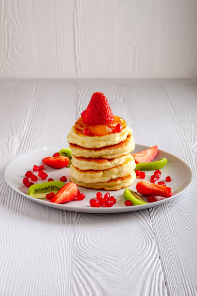 Stack of hot flapjacks served with fresh strawberries and kiwi on white wooden table - 写真・画像