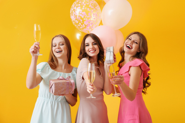 Gyönyörű fiatal nők pohár pezsgő és ajándékok a színes háttér - Fotó, kép
