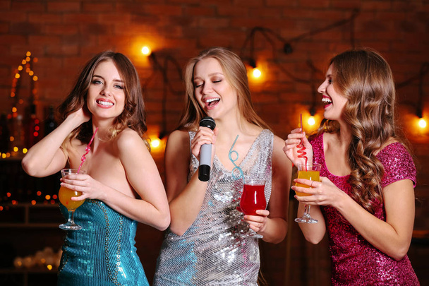 Belles jeunes femmes avec cocktails et microphone à la fête
 - Photo, image