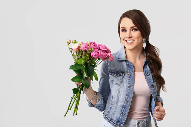 Mooie jonge vrouw met boeket van bloemen op lichte achtergrond - Foto, afbeelding