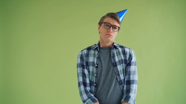 Portrait of unhappy young man in party hat looking at camera with sad face - Imágenes, Vídeo