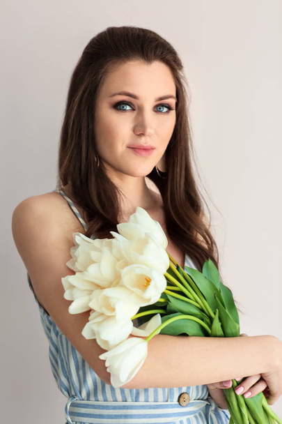 Beautiful young woman with bouquet of flowers on light background - Fotó, kép