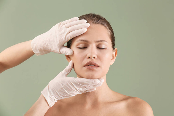Πλαστικός χειρουργός αγγίζοντας το πρόσωπο της νεαρής γυναίκας στο χρώμα φόντο - Φωτογραφία, εικόνα