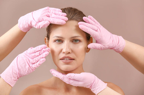 Schönheitschirurgen berühren Gesicht junger Frau auf farbigem Hintergrund - Foto, Bild