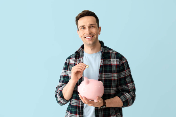 glücklicher junger Mann mit Sparschwein auf farbigem Hintergrund - Foto, Bild