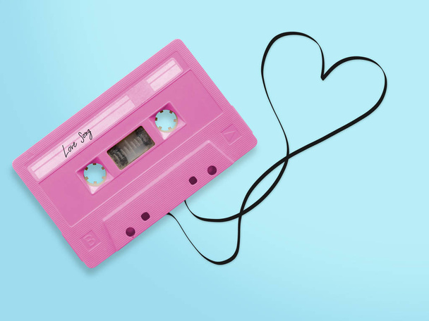 pink audio cassette tape with label tag love song tangled tape ribbon heart shape isolated on blue background, top view. - Foto, Bild