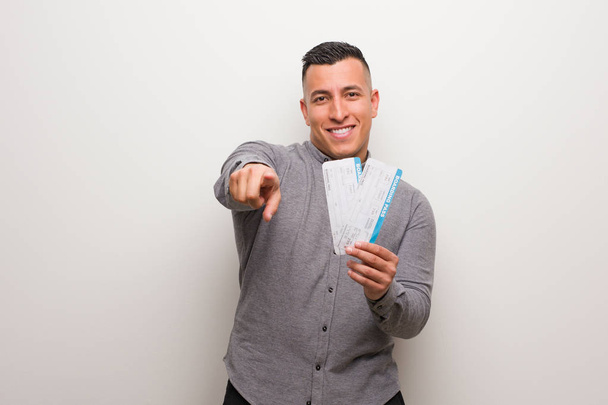 Joven latino sosteniendo un billete de avión alegre y sonriente apuntando al frente
 - Foto, imagen