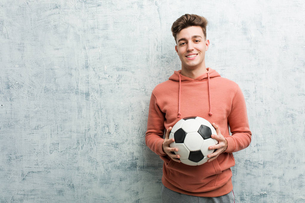 Giovane uomo sportivo che tiene un pallone da calcio felice, sorridente e allegro
. - Foto, immagini