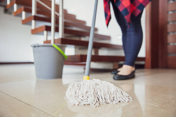 Woman is wiping the floor with mop with stairs in the background - Foto, imagen