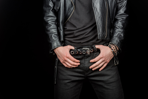 cropped view of man touching belt while standing isolated on black  - Foto, afbeelding