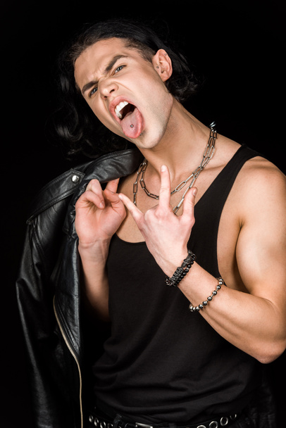 man showing rock sign and tongue while holding leather jacket isolated on black  - Fotografie, Obrázek