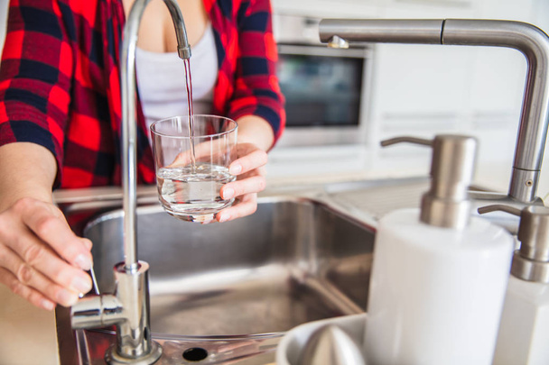 Woman is pouring water from the sink to the glass in the kitchen - Foto, imagen
