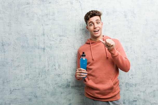 Joven deportista sosteniendo una bebida energética sonriendo alegremente señalando con el dedo índice de distancia
. - Foto, imagen