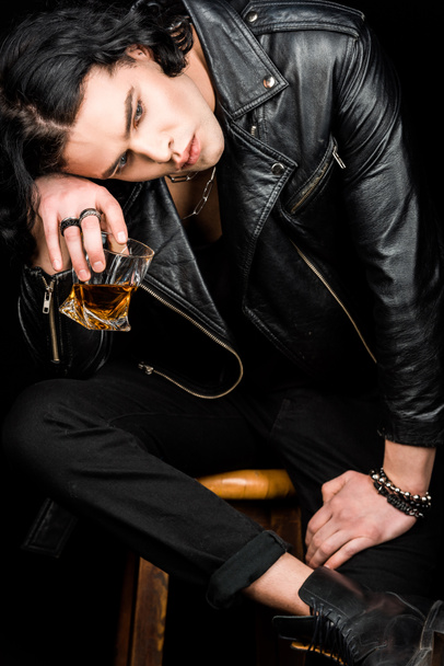 грустный мужчина сидит на стуле и держит стакан виски изолированный на черном
   - Фото, изображение