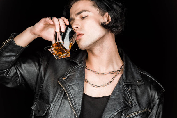 pohledný muž v koženém kabátku pít whisky izolovaná na černém  - Fotografie, Obrázek