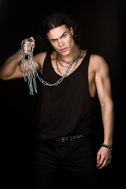 angry man looking at camera and holding chains isolated on black  - Photo, Image