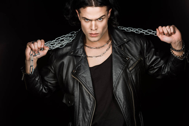 serious man looking at camera and holding metallic chains isolated on black  - Foto, Imagen