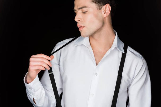 young man in white shirt touching suspenders isolated on black  - Photo, Image