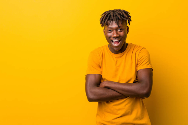 Jonge zwarte man dragen rasta 's over gele achtergrond lachen en plezier hebben. - Foto, afbeelding