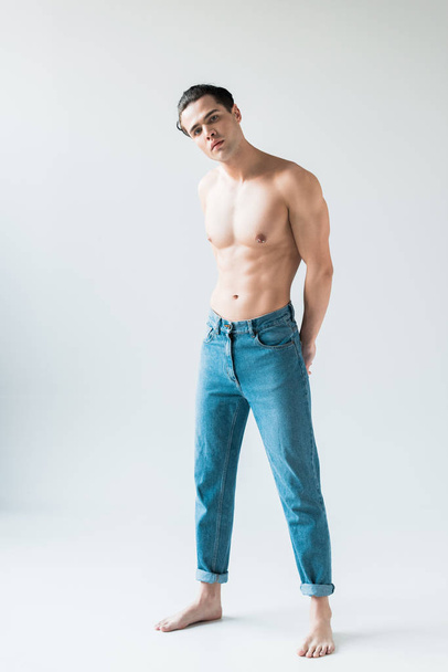 handsome shirtless man standing in blue jeans and looking at camera on white  - Photo, Image
