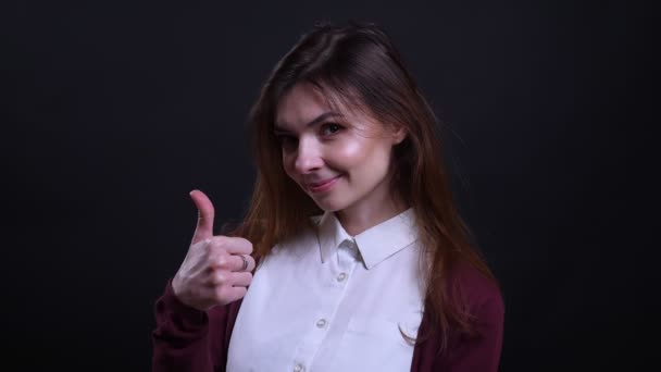 Portrait of young brunette businesswoman puts her thumb up to show like and respect on black background. - Footage, Video