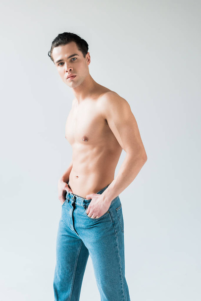 handsome man touching blue jeans while standing on white  - Foto, immagini