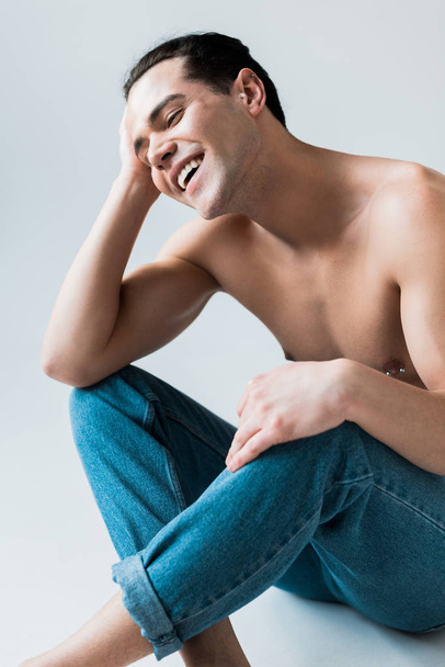 счастливый и без рубашки мужчина сидит в синих джинсах на белом
  - Фото, изображение