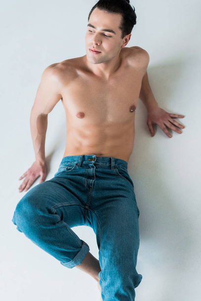 overhead view of muscular and shirtless man lying in blue jeans on white  - Photo, Image