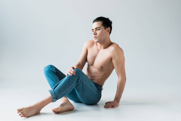 handsome man posing while sitting in blue jeans on white  - Foto, immagini