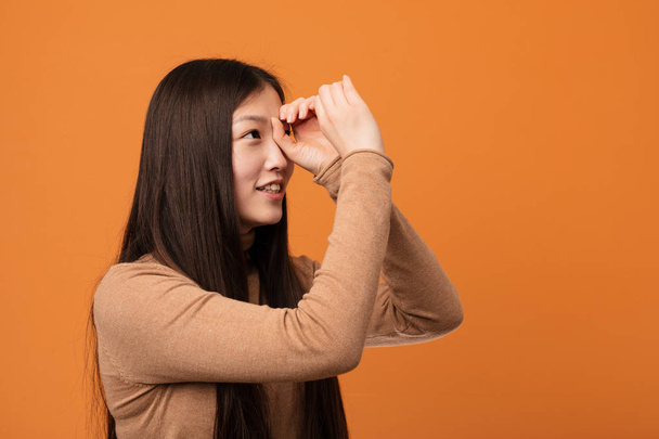 Jovem mulher chinesa bonita olhando para longe mantendo-o mão na testa
. - Foto, Imagem