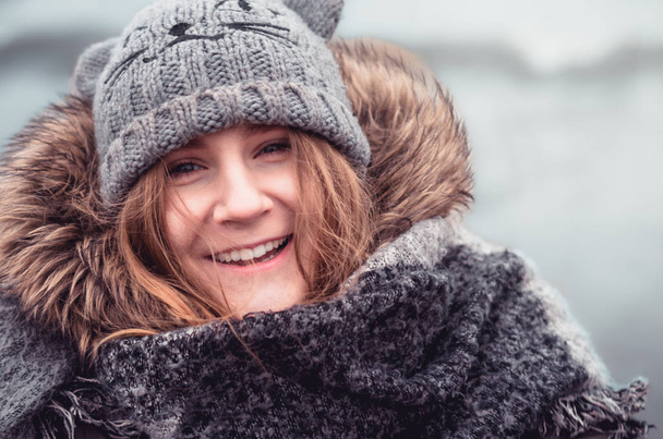 Ładna wesoła dziewczyna w ciepłym zimowym ubraniu uśmiechnięta do aparatu. - Zdjęcie, obraz