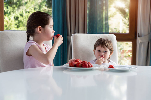 Cute children eating fresh ripe strawberries at home - Photo, Image