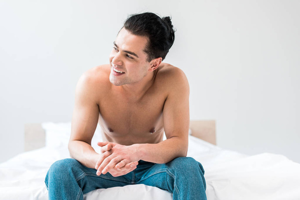 homem feliz sorrindo enquanto sentado na cama com as mãos apertadas
  - Foto, Imagem