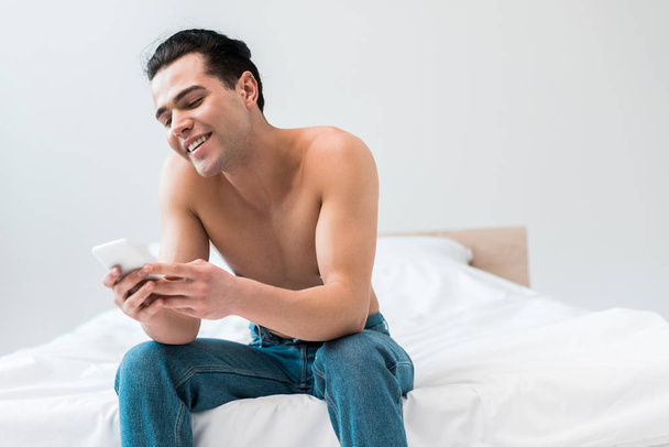 happy shirtless man looking at smartphone while sitting on bed at home  - Фото, зображення