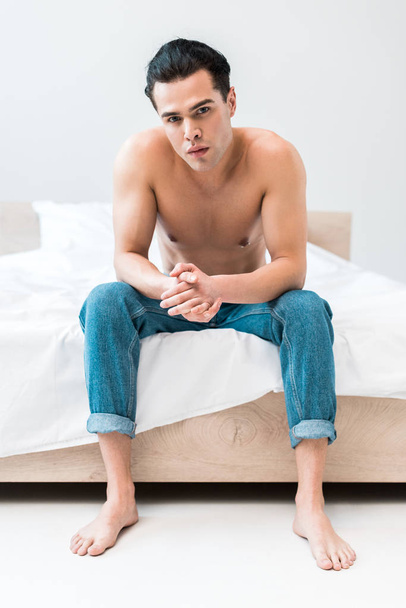 handsome and muscular man sitting on bed with clenched hands  - Photo, image