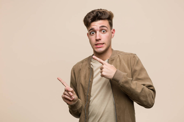 Young caucasian man wearing a brown jacket shocked pointing with index fingers to a copy space. - Photo, Image
