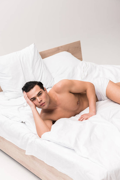 serious muscular and shirtless man looking at camera and lying on bed  - Foto, Imagem
