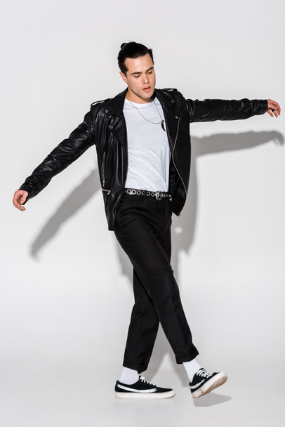 handsome and stylish man in leather jacket walking with outstretched hands on white  - Фото, зображення