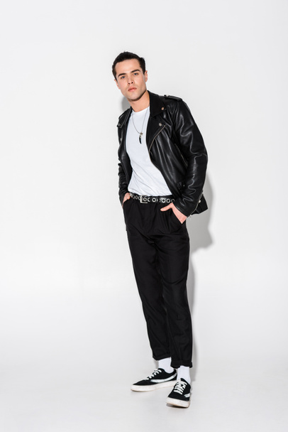 stylish man in leather jacket standing with hands in pockets on white  - Фото, изображение