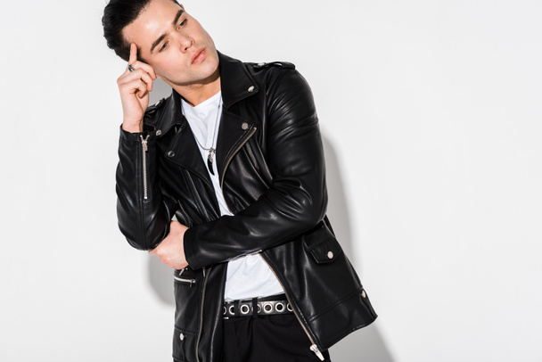 pensive and stylish man in leather jacket standing on white  - Foto, afbeelding